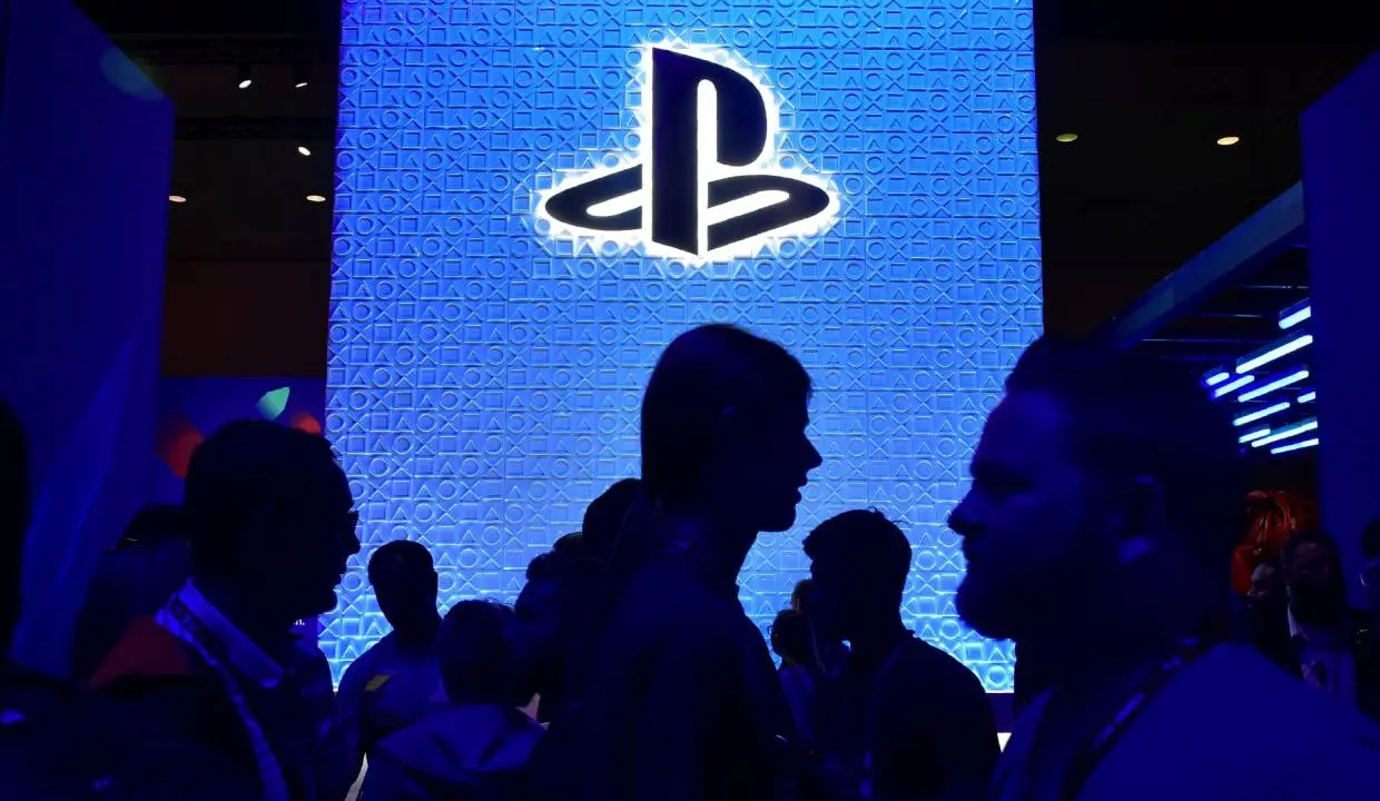 Stand da PlayStation durante uma conferência da E3 enquanto várias pessoas passam na frente do logo da marca.