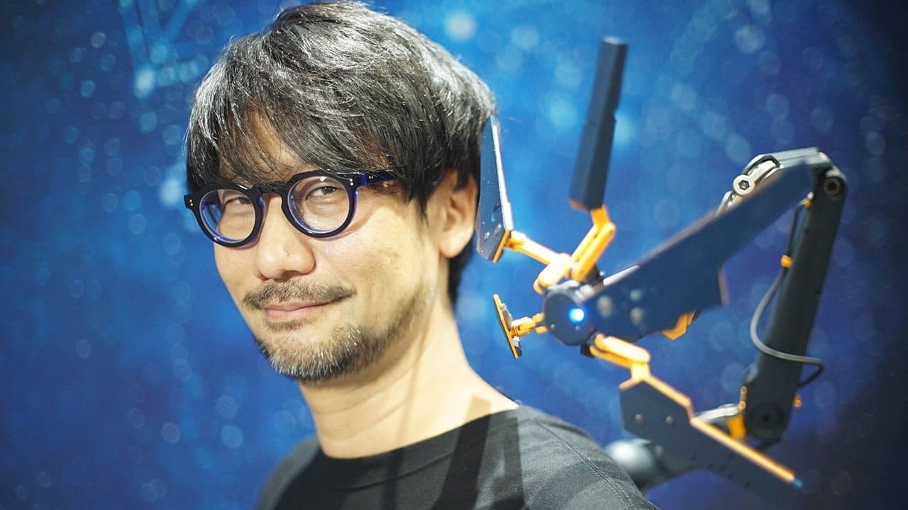 Imagem do diretor Hideo Kojima, dono da Kojima Productions, sorrindo e com um acessório de Death Stranding