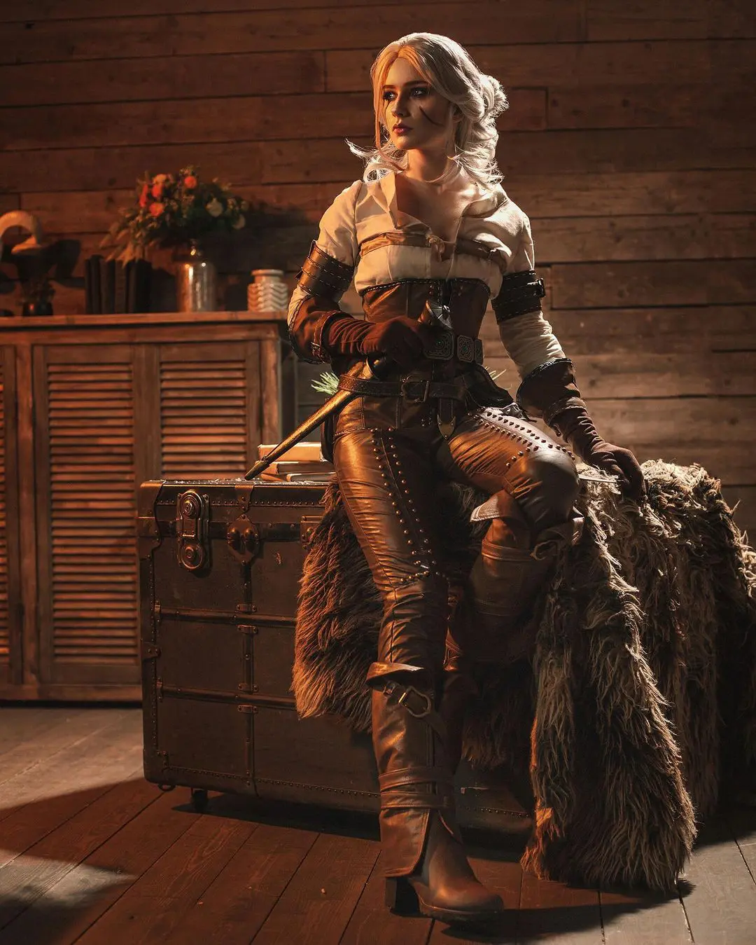 Imagem do cosplay da personagem Ciri, de The Witcher 3, sentada em cima de um baú