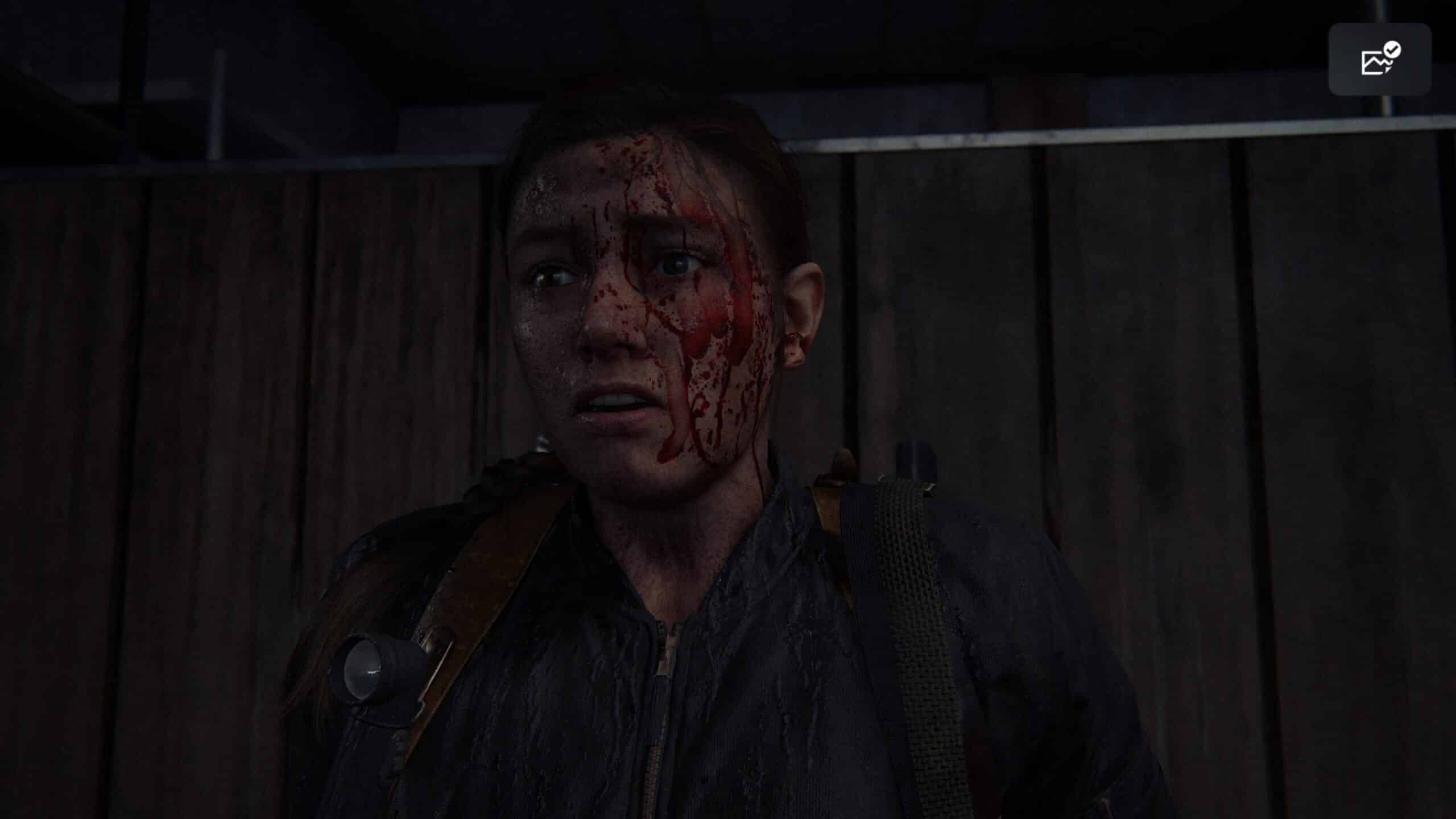 Abby, personagem de The Last of Us 2, com o rosto todo ensaguentado em um ambiente escuro