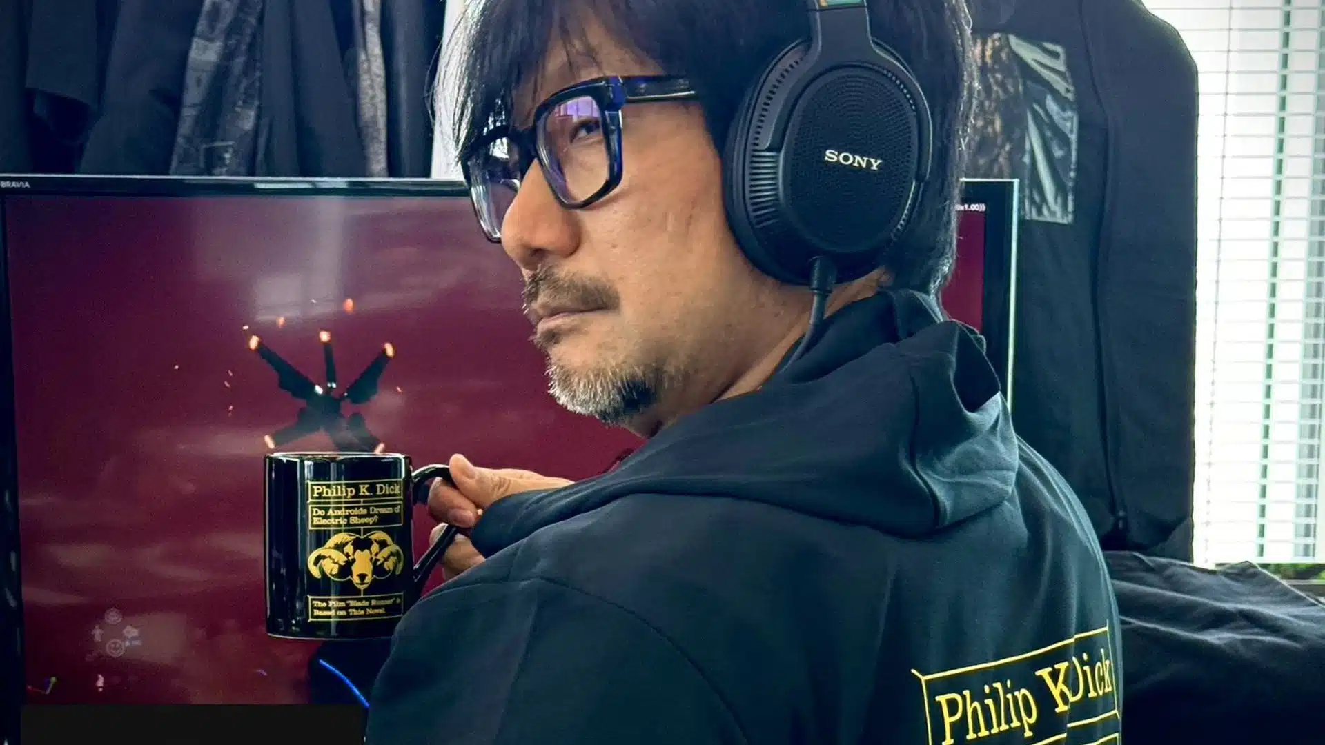 Hideo Kojima em seu escritório tomando algo na caneca